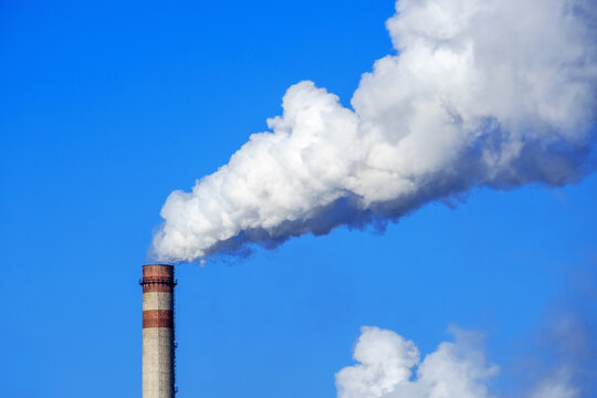 White smoke and steam from a high chimney of a power plant against a bright blue