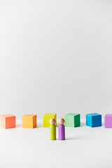 Wooden figures concept. Couple standing in front of wooden blocks in colours of the gay pride rainbow flag. Couple of white skin colour. 