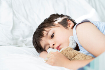 Obraz na płótnie Canvas Kid 7 year old lying on bed, Sleepy child waking up the morning in his bed room with morning light, Cute little boy sleeping with his dog toy in bed. Children health care or Sleep problems in young