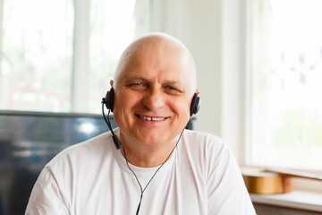 Elderly man with headphones and computer laughing happily, telework, e-business or commerce,...