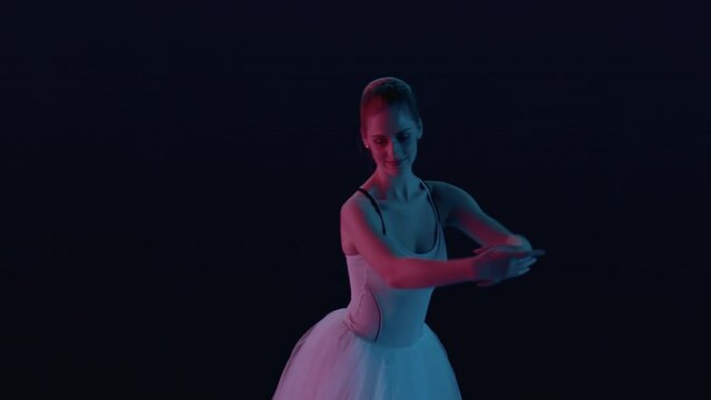 View of ballerina performing classical dance moves on stage in creative lighting