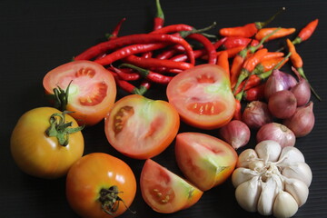 A few of portion cut tomatoes, garlic, and red chilies on black table.