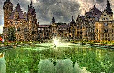 Fototapeta na wymiar View on a castle form the perspective of small pond with fountain.