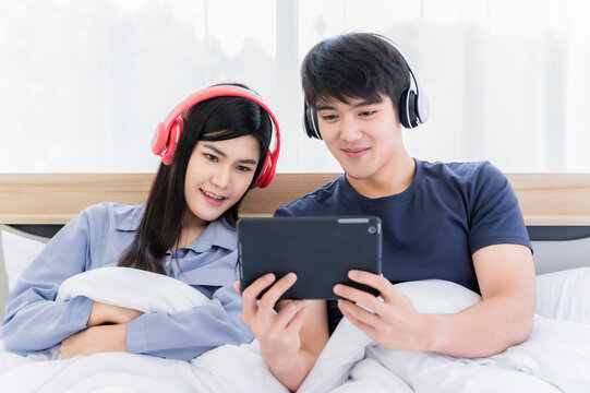 Young couple wear headphone and listening music by smartphone on bed in bedroom