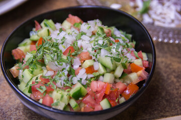 Fresh Israeli vegetables salad, containing cucumber, tomato white onion and parsley, served in a dark bowl 