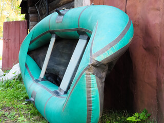 a green rubber boat leaning on a shed.