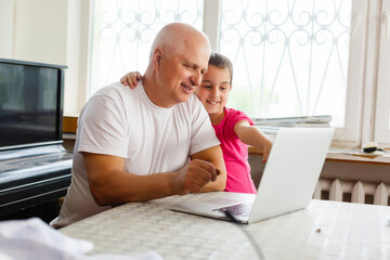 Portrait of grandfather and granddaughter doing homework with laptop.