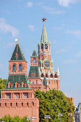 Fototapeta na wymiar View of Spasskaya Tower of Moscow Kremlin above trees on a summer morning. Blue sky with few clouds in the background. Theme of travel in Russia.