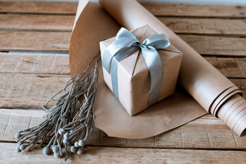 gift with a silver bow on a wooden table with craft paper and a flower