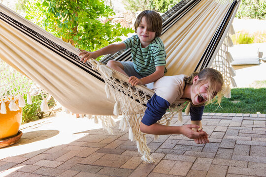 teen girl and her younger brothewrplaying in hammock