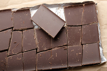 Dark chocolate bar broken into pieces laying in a foil on paper wrap