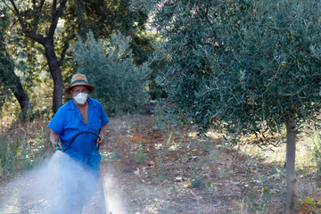 man in a hat and protective mask spraying a field of trees