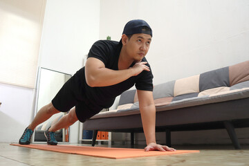 Asian male doing exercise at home to stay healthy on new normal lifestyle, indoor home workout, shoulder tap push ups plank position