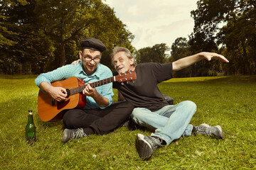 Two men on city park summer meadow enjoying day with guitar