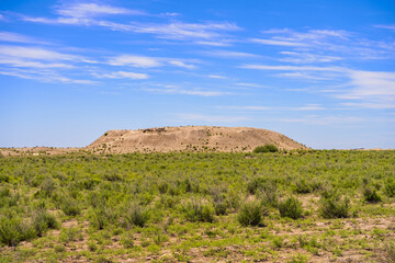 Turkic mound in the steppe. Burial ground of ancient Türks. Historical places. Burial place of the Turks near the ancient settlement. Barrow in the Kazakh steppe. Clouds in the blue sky