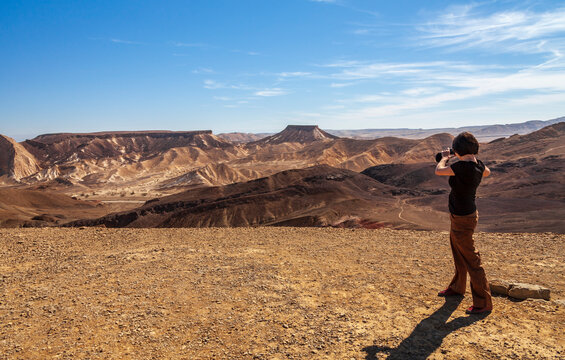 A girl on top of a mountain photographs a mountain landscape on camera. Ramon Crater, Israel. Travel concept and photos.