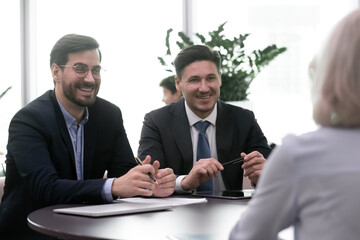 Smiling business people discuss positive results during meeting with partner or consultant. Two successful businessmen happy listen to financial advisor or candidate on job interview