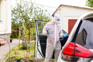 Man wearing a personal protective equipment suit, gloves, surgical mask and face shield, testing covid-19 coronavirus on another man sitting in a car.