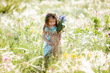 portrait of a cute little girl with a wreath on her head smiling holding wildflowers of cornflower