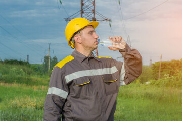 An engineer drinks water on a hot summer day, a worker rests near a high-voltage line. Industry. Energy.