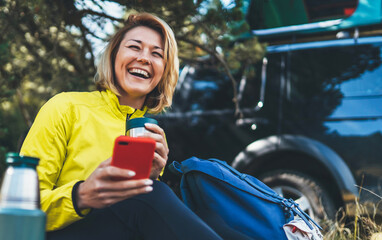 Happy tourist talking on cellphone drinks tea while traveling. woman smile showing teeth calling on internet mobile phone summer green forest. Joy girl using smartphone have fun emotion in outdoors