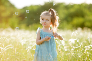 Little girl inflates soap bubbles in summer on a walk