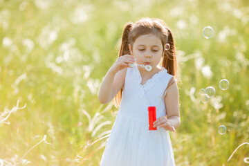 Little girl inflates soap bubbles in summer on a walk