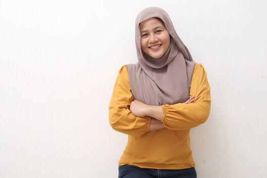 Portrait of Asian muslim woman wearing hijab smiling friendly with crossed arms, confident gesture, successful businesswoman