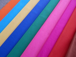 Rolls of colourful striped textiles in many colours in the diagonal position across the frame.