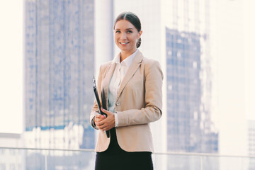 Portrait beautiful successful business woman in suit hold documents folder and smile outdoors. Attractive young corporate girl with clipboard in hand on city street. Female entrepreneur, lawyer person