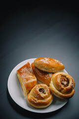 Vertical shot of delicious sesame buns or pies on white plate on black wooden table background. Tasty unhealthy snack for lunch. Overweight, diet, nutrition, eating habits concept. Copy space.