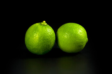 Two natural limes, close-up on a black background. Fresh citrus fruits.