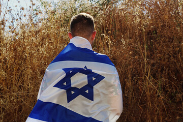 Jewish young  man stands an Israeli field with the flag of Israel on the back. Concepts: patriotic...