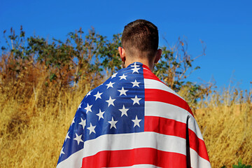 American boy is standing on an American field with the USA flag on his shoulders. Concepts:...