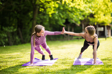 Two fit sporty women giving high five to each other while doing push up on exercise mat in the park