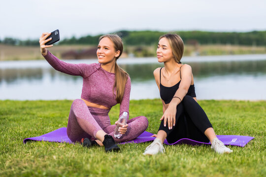Cute two girls taking a selfie with their phone while they do some yoga at a park