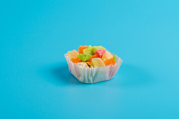 A portion of candied fruit in a paper muffin cup on a blue background.