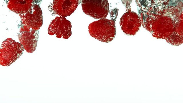 Super slow motion of falling raspberries into water on white background. Filmed on high speed cinema camera, 1000 fps.