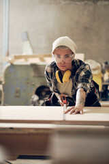 Female carpenter measuring plank with tape