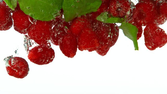 Super slow motion of falling raspberries into water on white background. Filmed on high speed cinema camera, 1000 fps.