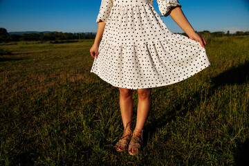 Closeup woman legs on grass background.Young girl legs in a light dress at sunset on a green grass...