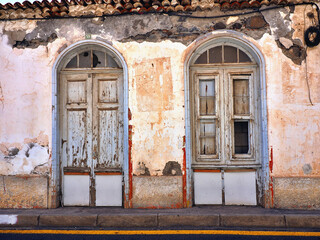 Front view of an old, dilapidated and rundown old town house in "San Sebastian" on "La Gomera" (Canary Island). crumbling plaster and two arched entrance doors with dilapidated formerly white wooden s