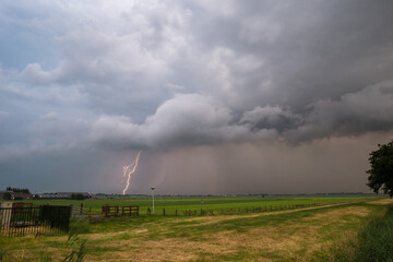 Fototapeta na wymiar Severe thunderstorm approaching over a field. Lightning bolt hits the earth.