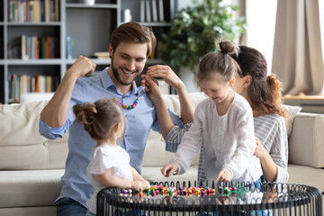 Happy young family making colorful wooden beads jewelry together, smiling father holding handmade...