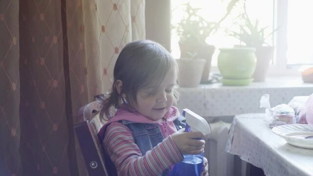 Little girl plays in the kitchen with a spray of water, laughs and rejoices