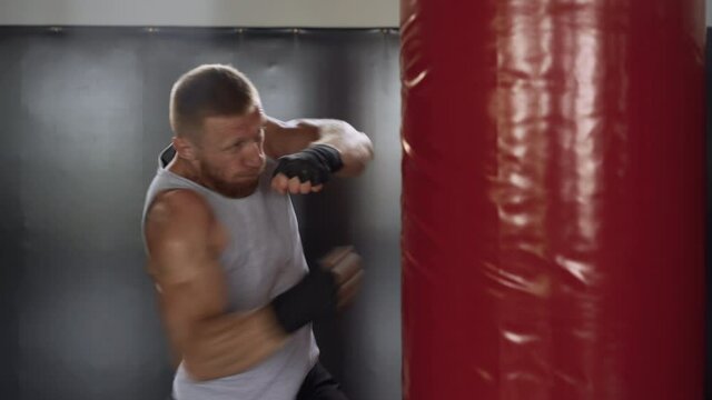 Boxer training gym punching bag Man kickboxer boxing, workout indoor. Cardio exercising preparing for fight. Aggressive mix fighting. Middle adult caucasian guy fight with red foam rubber column 