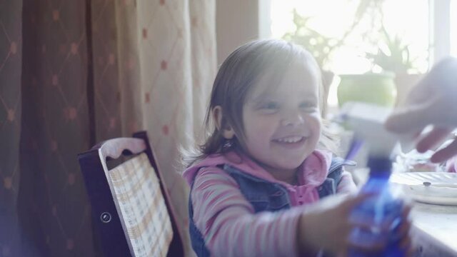 A little girl plays in the kitchen, mom pours water on her with a spray bottle