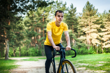 Naklejka premium Portrait of a young man moving on a Bicycle. In a public Park, among trees and vegetation.