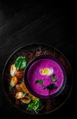 Cold beetroot soup with sour cream, egg and hot potatoes in bowl on black wooden table background
