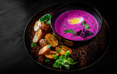 Cold beetroot soup with sour cream, egg and hot potatoes in bowl on black wooden table background